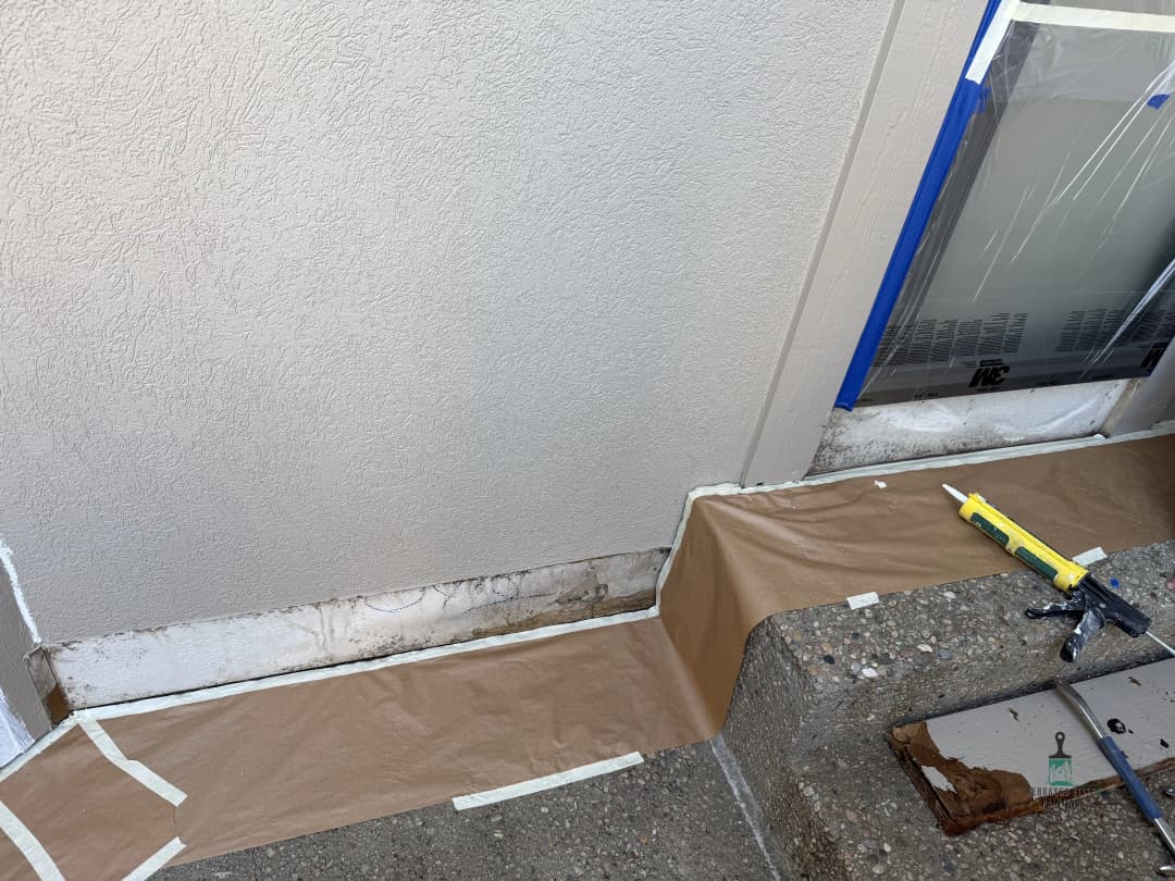 Exterior wall prep for painting, featuring protective tape and paper, and visible water damage.