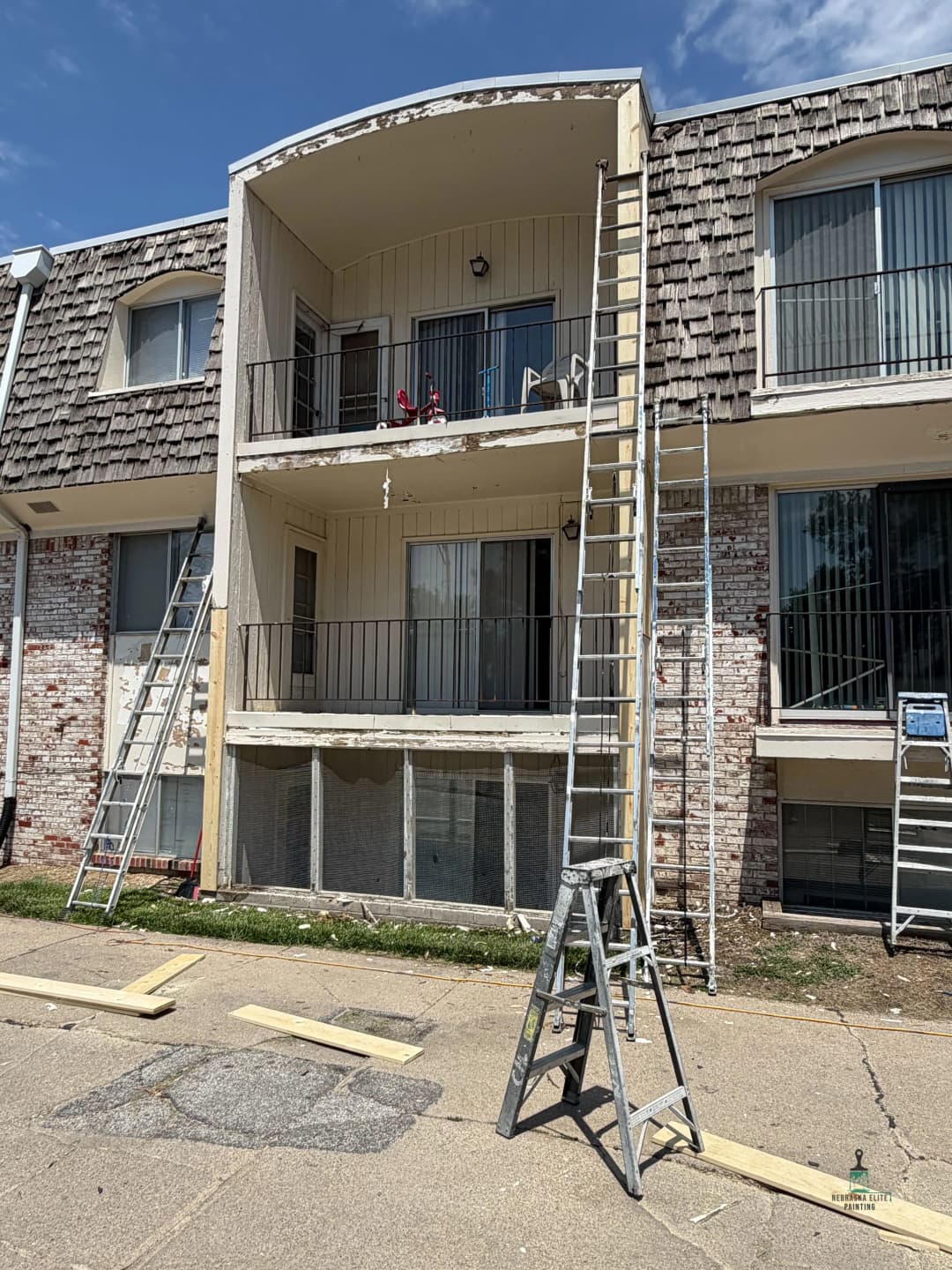 Two-story apartment building with ladders, scaffolding, and renovation materials outside.