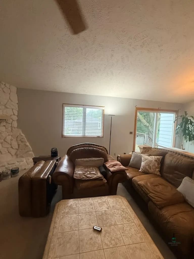 Cozy living room with leather sofas, stone fireplace, and large windows for natural light.