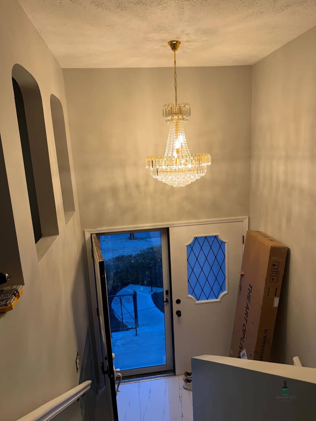 Elegant chandelier illuminating a modern staircase, leading to a front door.