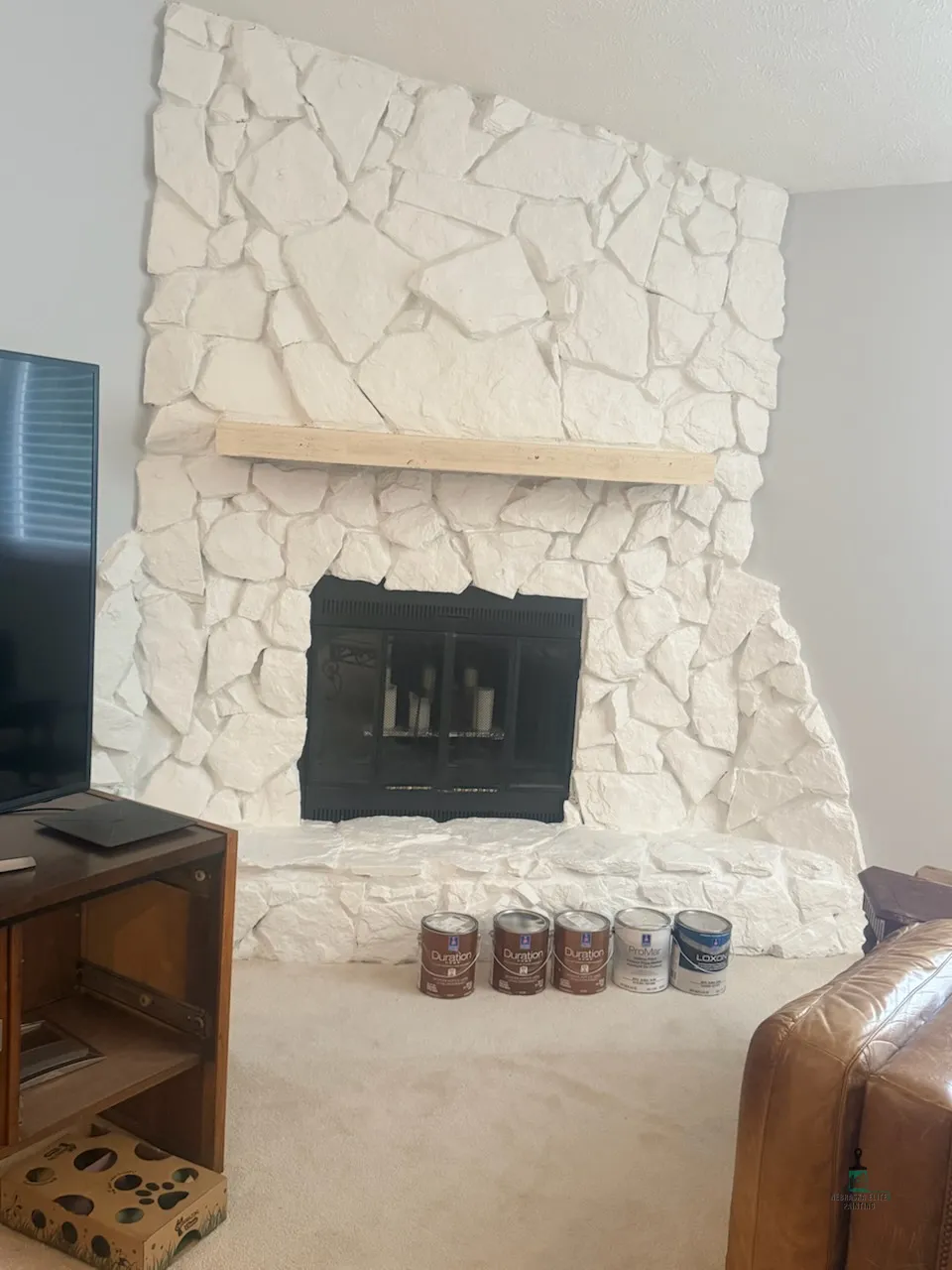 Modern white stone fireplace with wooden mantel and paint cans in a cozy living room setting.