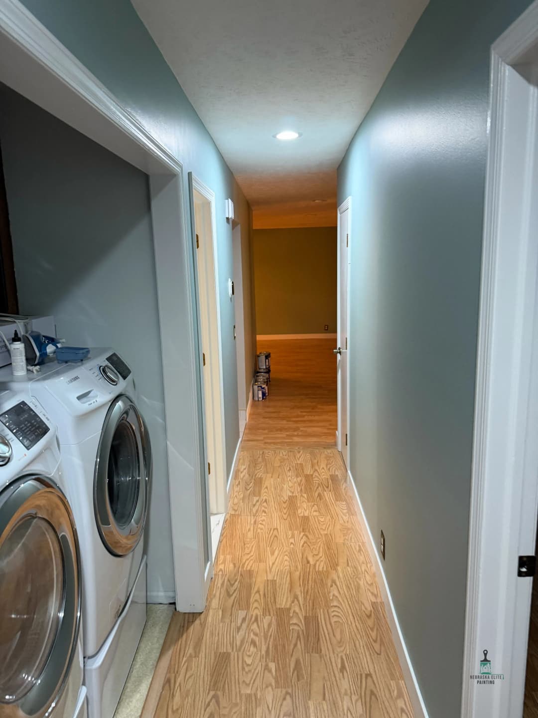 View of a hallway with laundry machines on the left and a green wall at the end.