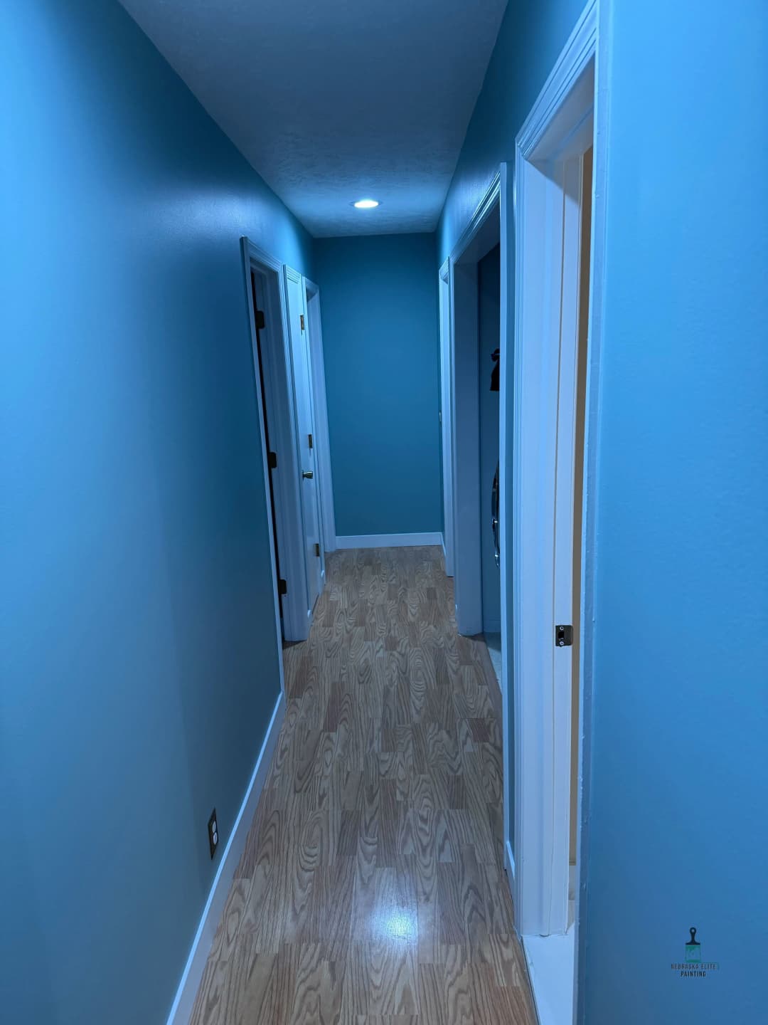 Bright blue hallway with light wood flooring and closed doors on either side.