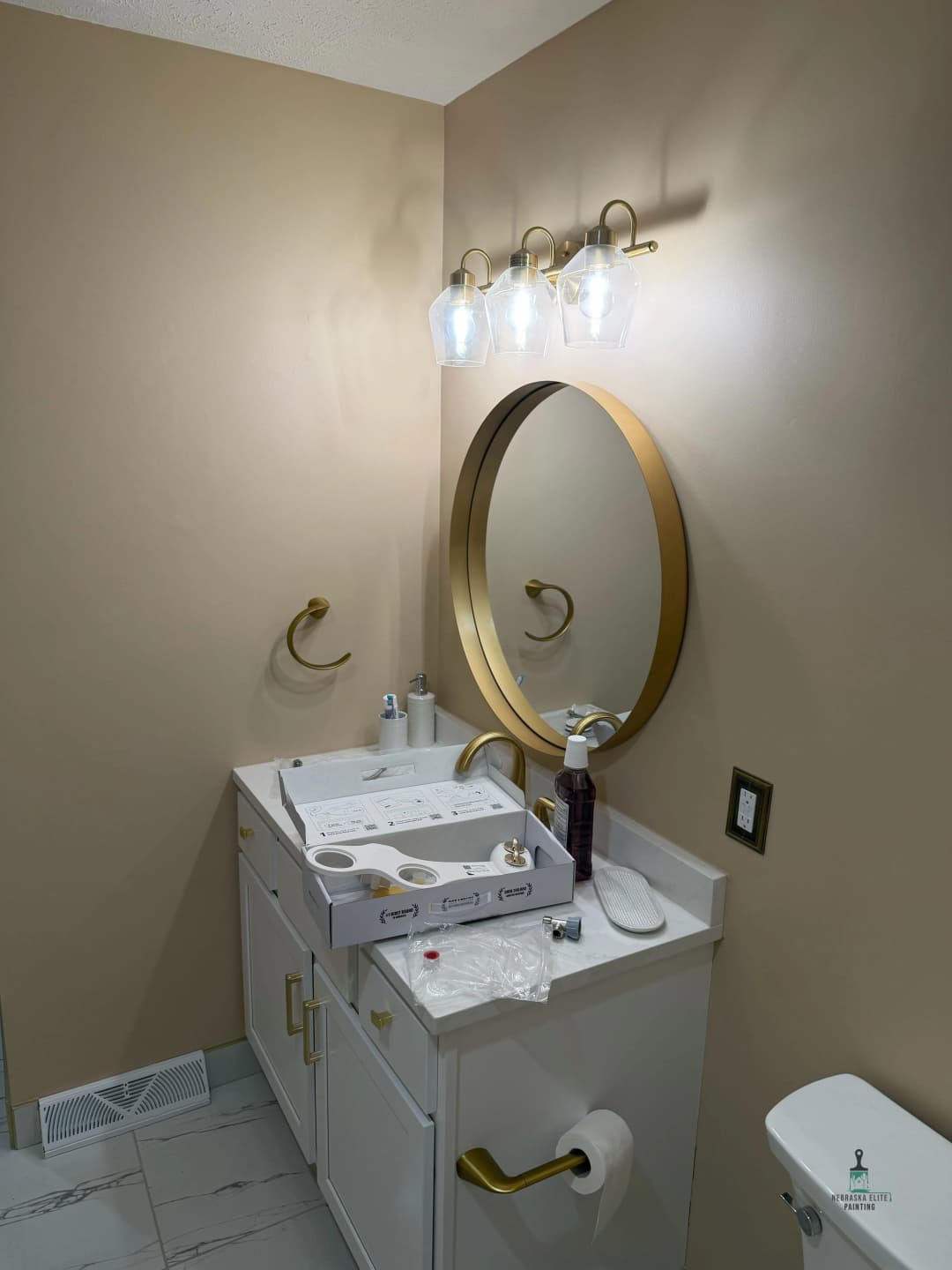 Modern bathroom vanity with gold accents, round mirror, and stylish lighting fixtures.