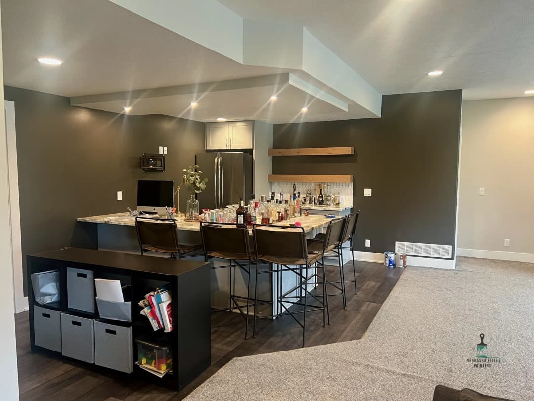 Modern kitchen bar with seating, dark walls, and an organized countertop displaying various beverages.