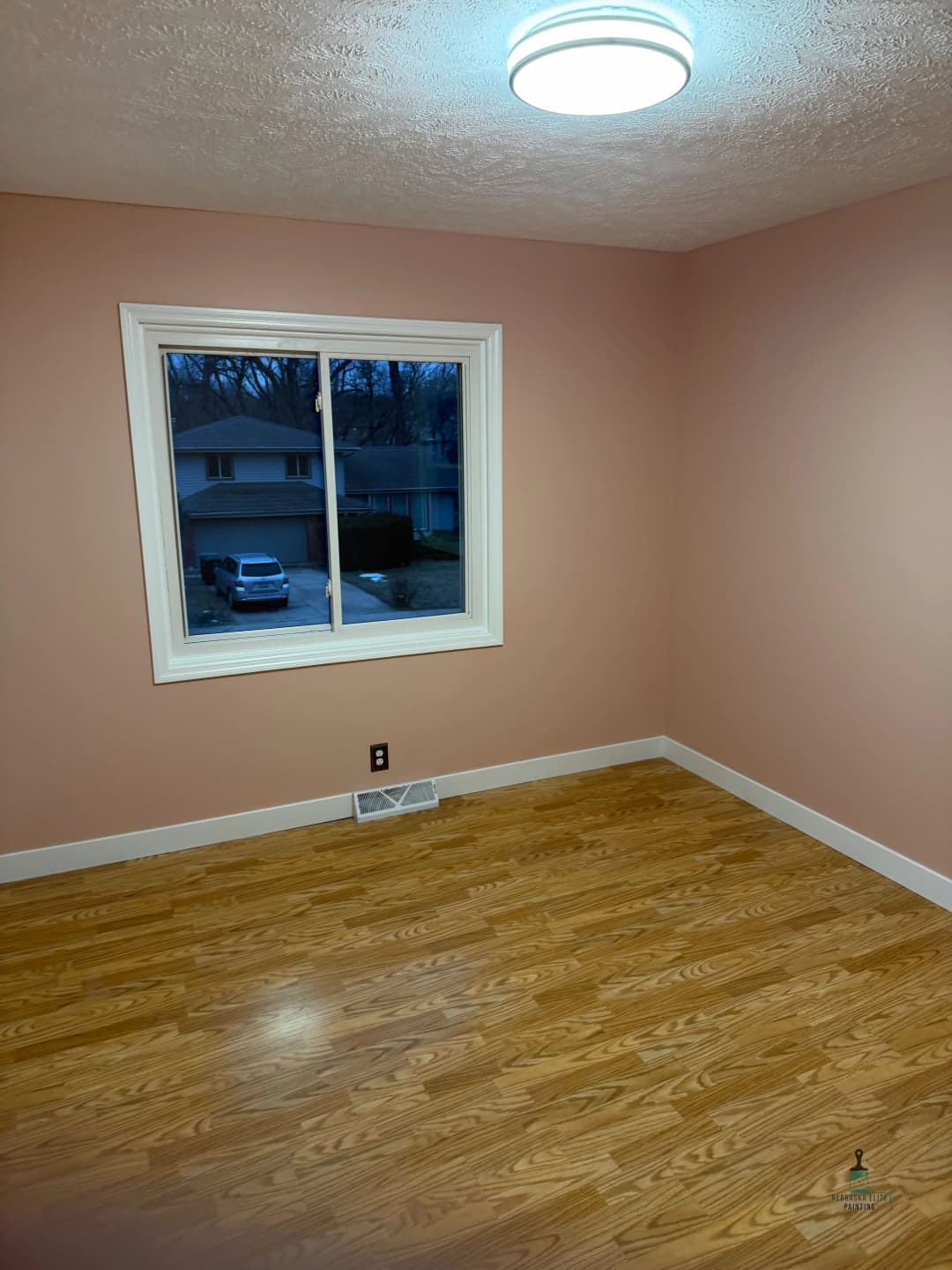 Empty room with pink walls, hardwood floor, window, and ceiling light. Ideal for decoration.