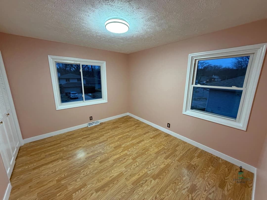 Cozy pink bedroom with large windows and hardwood floors, perfect for natural light.