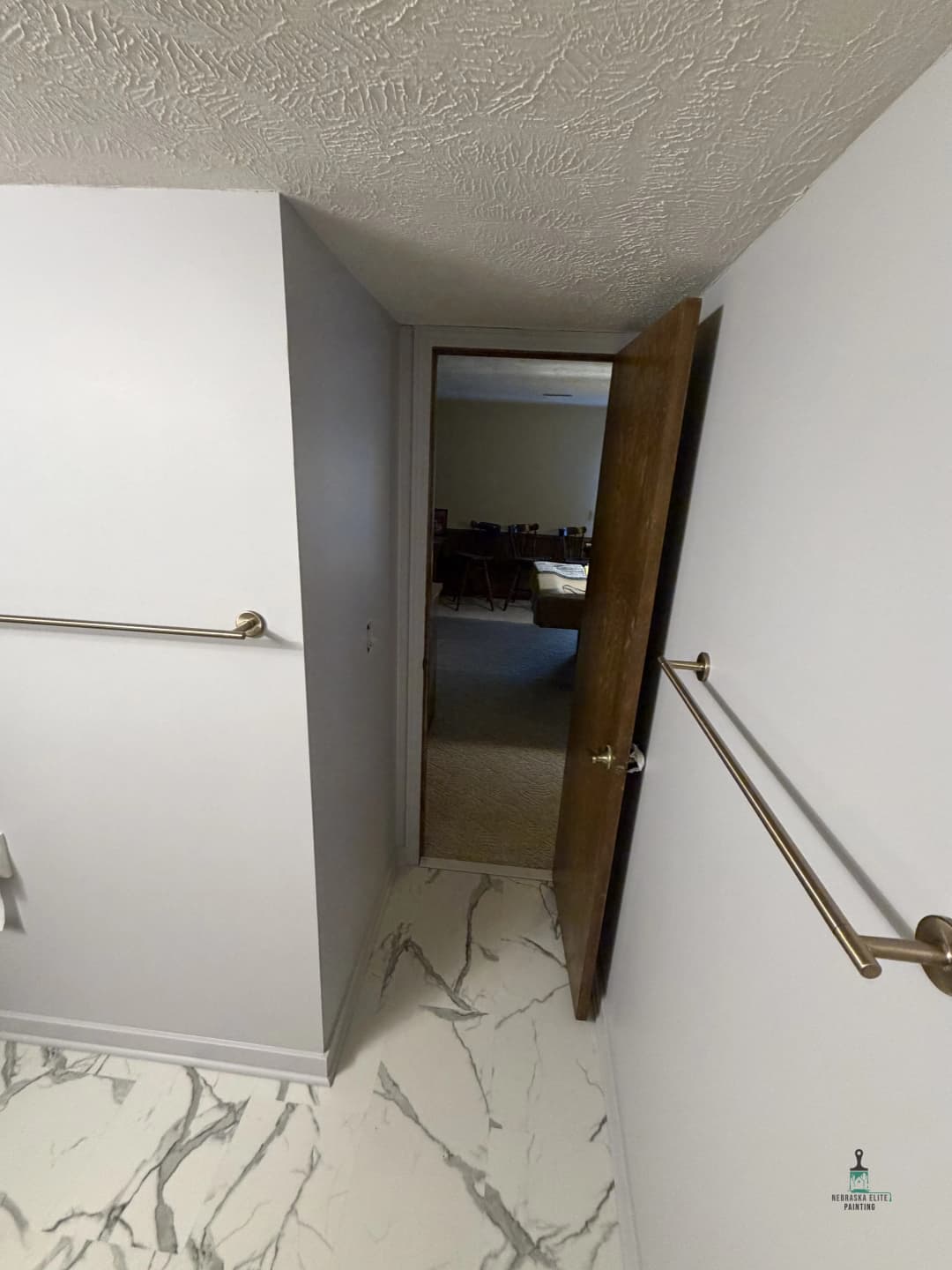 Open door leading to a room, featuring marble flooring and towel bars on the wall.