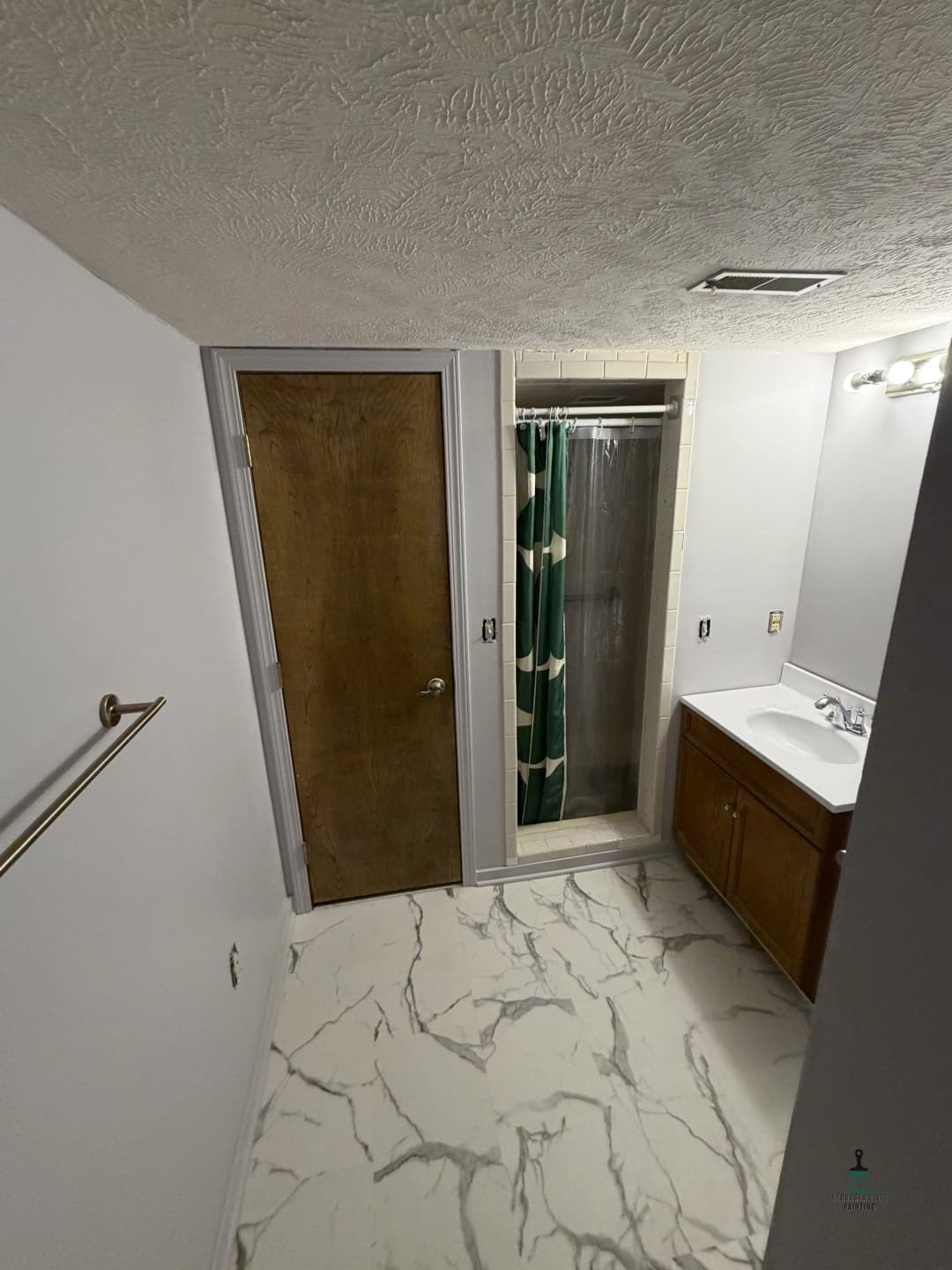 Spacious bathroom with shower, wooden door, and marble-patterned flooring.
