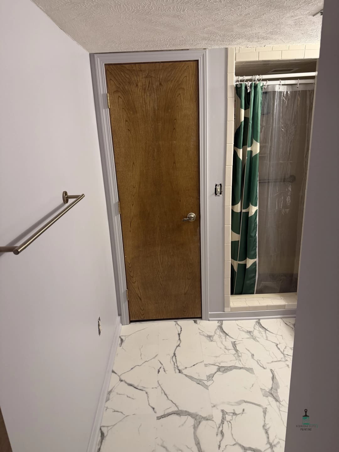 View of a bathroom interior featuring a wooden door, shower curtain, and marble floor tiles.