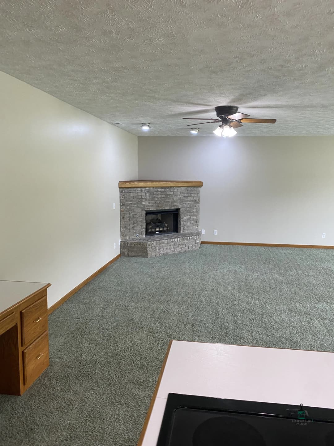 Spacious living room with gray carpet, ceiling fan, and stone fireplace.