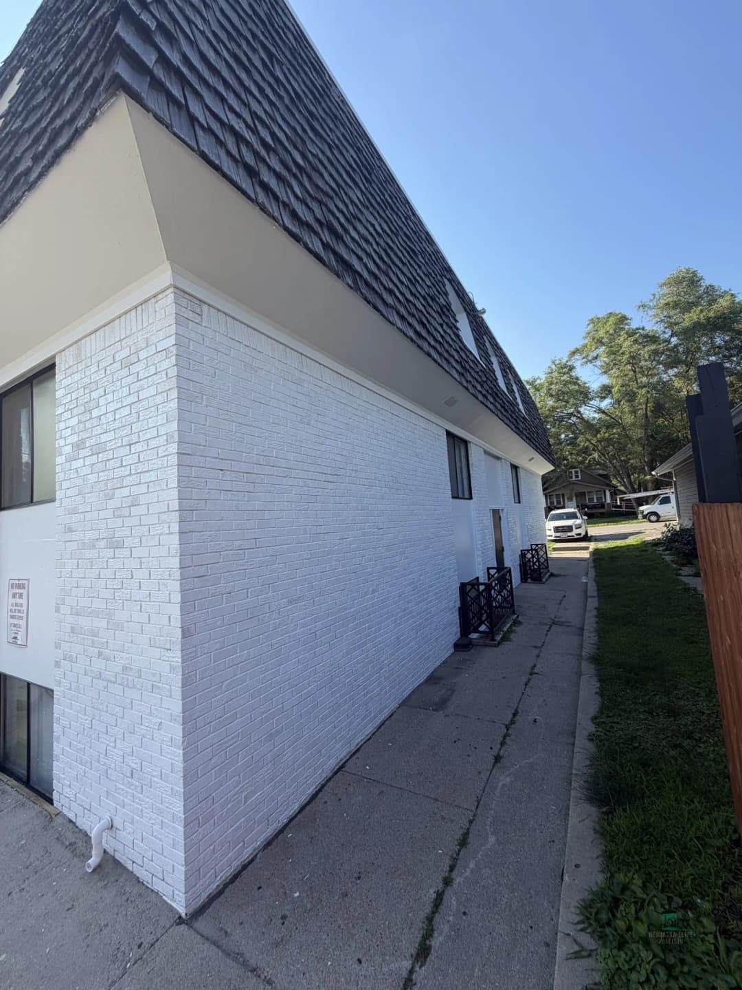 White brick building with a steep, shingled roof and clear blue sky overhead.