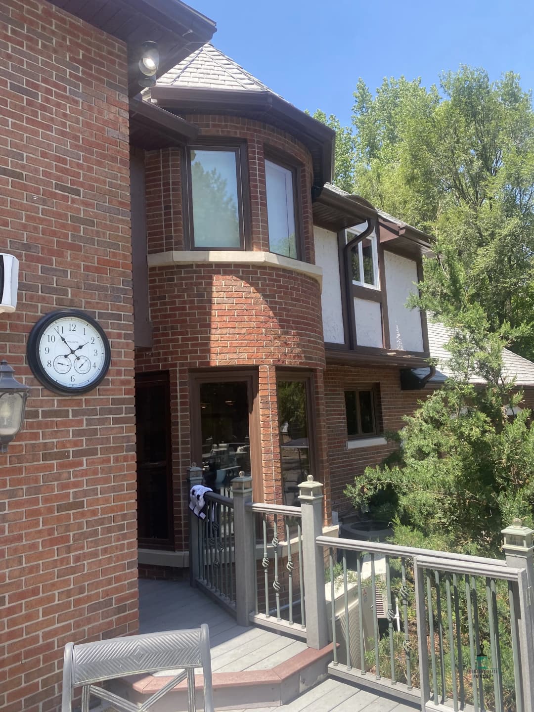 Brick house with large windows, balcony, and garden view under clear blue sky.