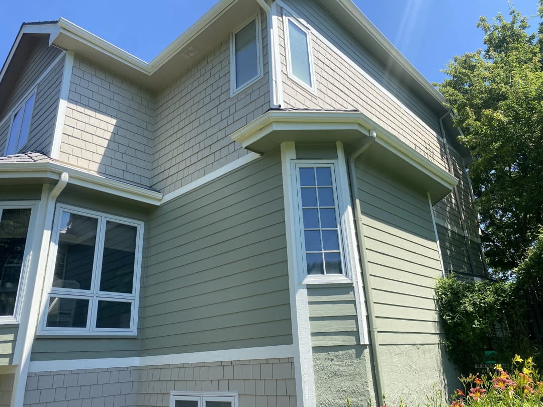 Green residential house exterior with windows and detailed siding under bright blue sky.