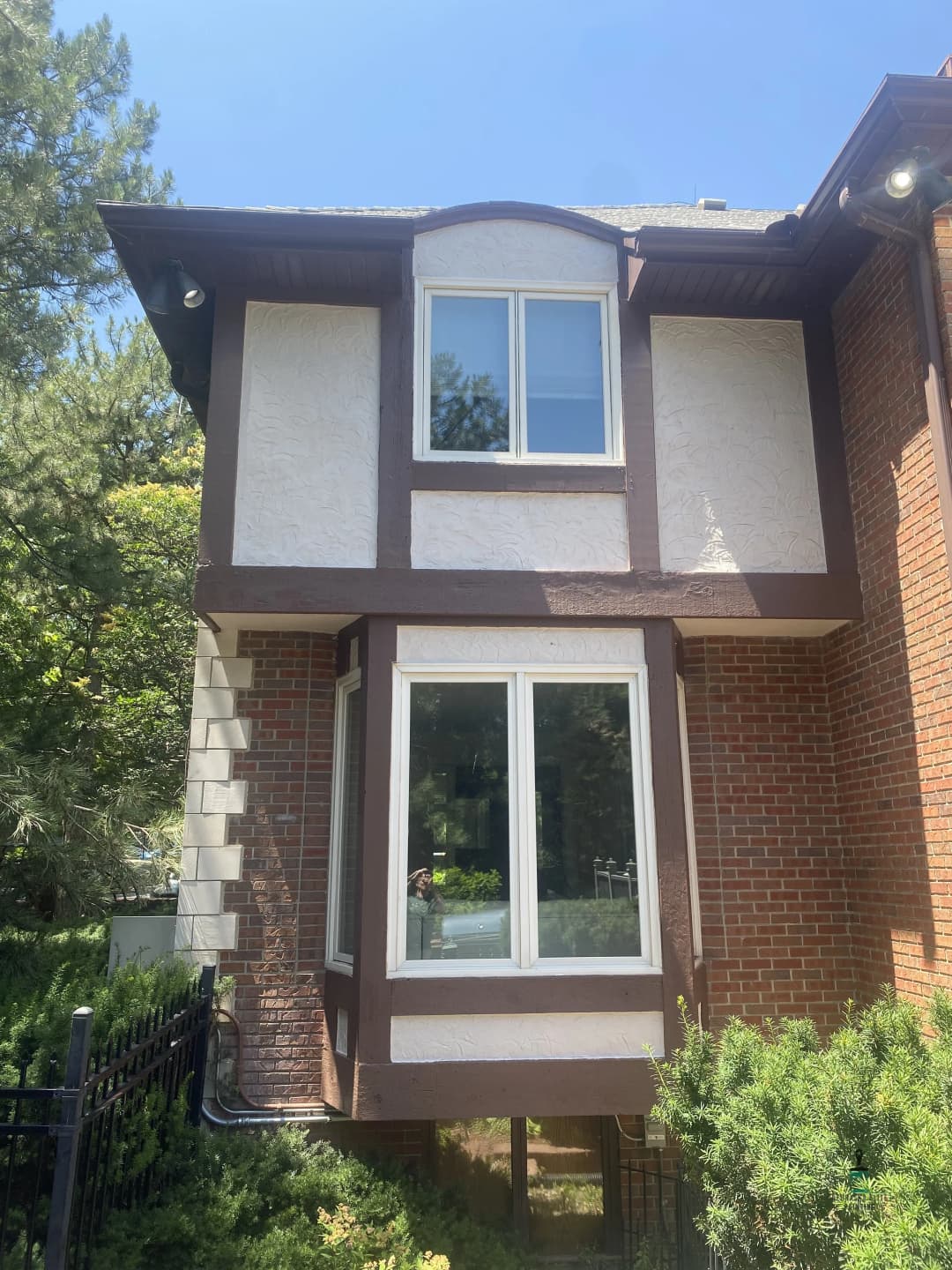 Two-story house exterior featuring a mix of brick and textured siding, with large windows.