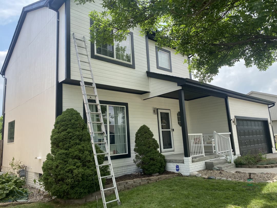 Exterior view of a two-story house with a ladder, manicured lawn, and front porch.