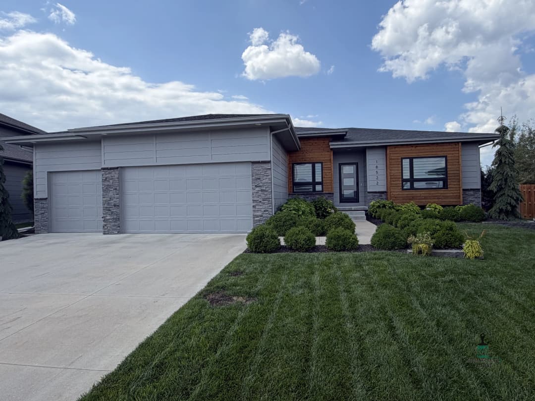 Modern home with stone accents, double garage, and landscaped front yard under a cloudy sky.