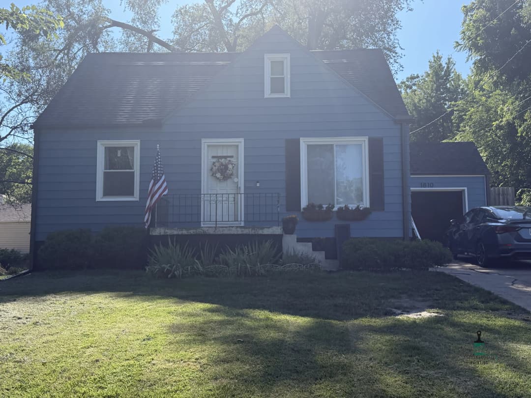 Blue house with porch, American flag, and well-maintained front yard on a sunny day.