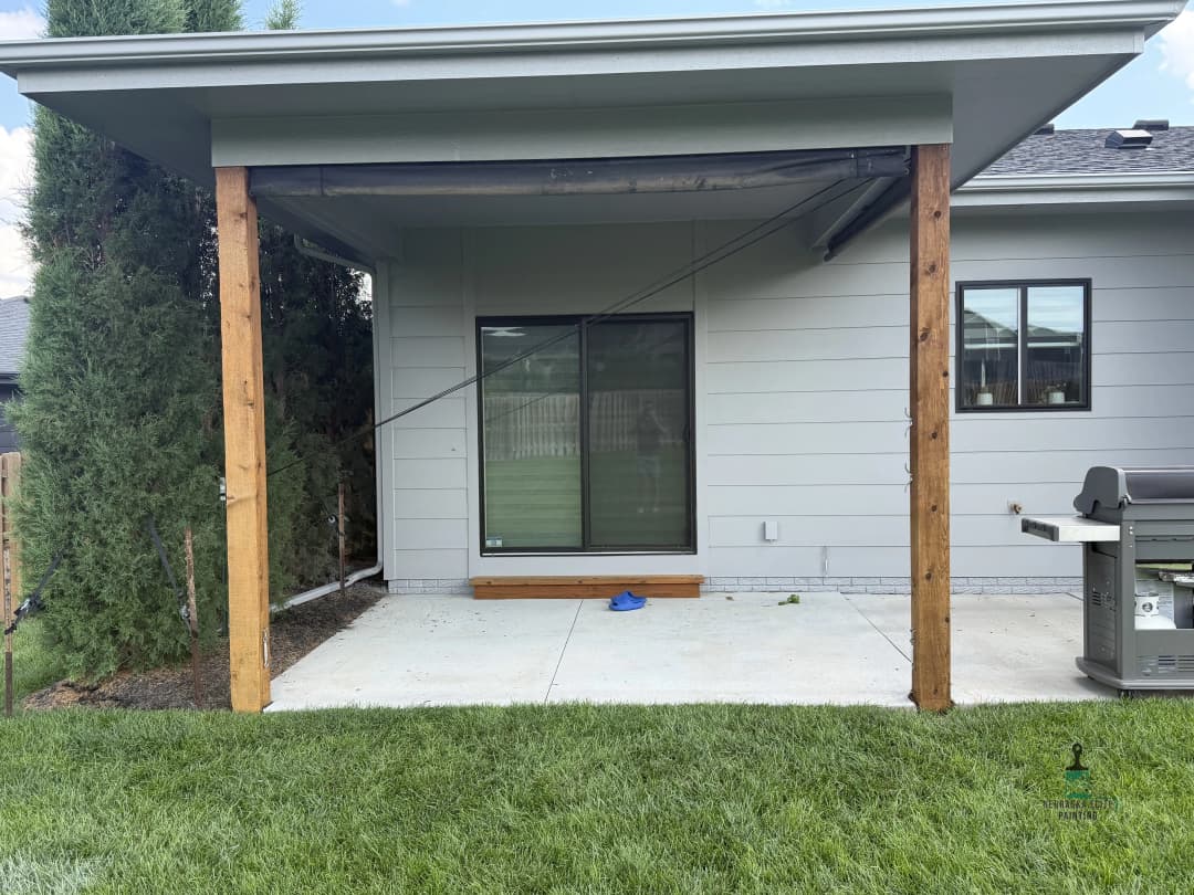 Patio area with wooden posts, grill, and sliding door on a grassy lawn, residential setting.