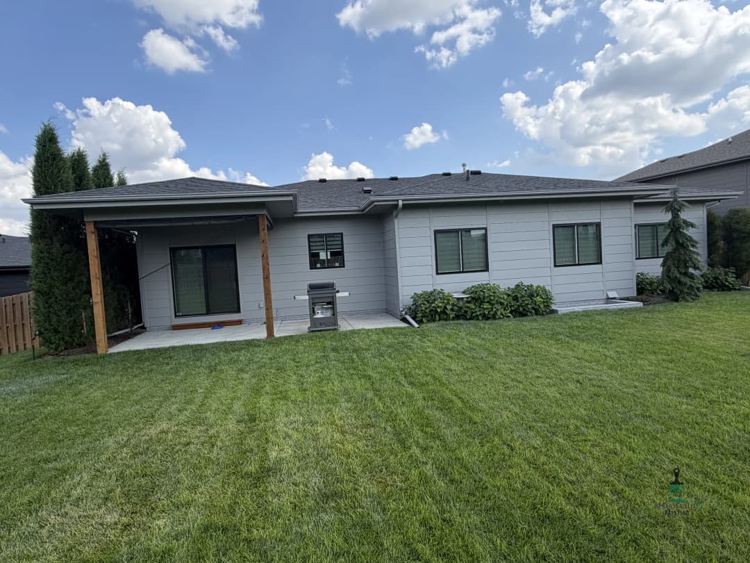 Modern home exterior with patio and green lawn under a cloudy sky.