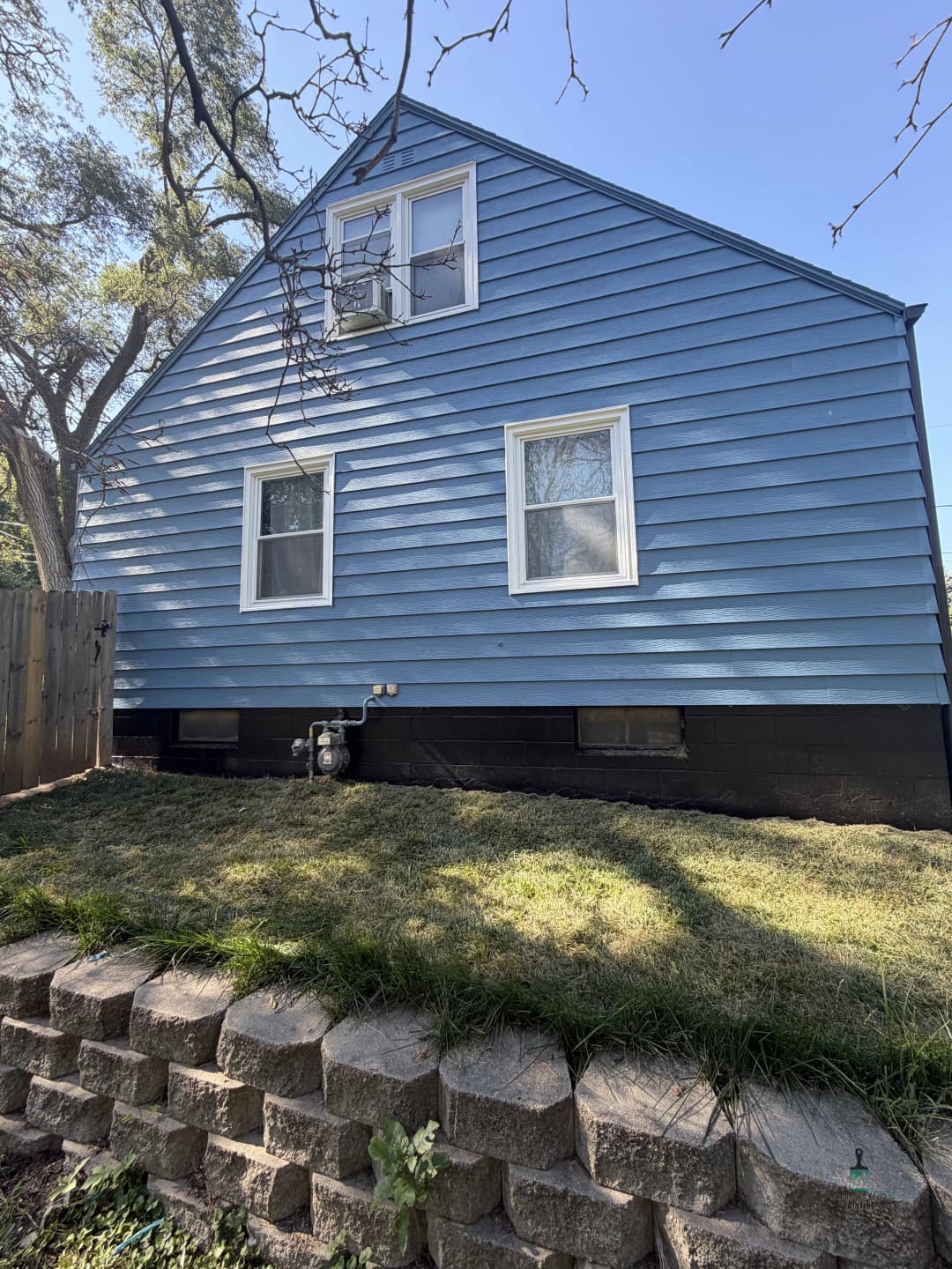 Blue house with a sloped roof, three windows, and a stone wall in the foreground.