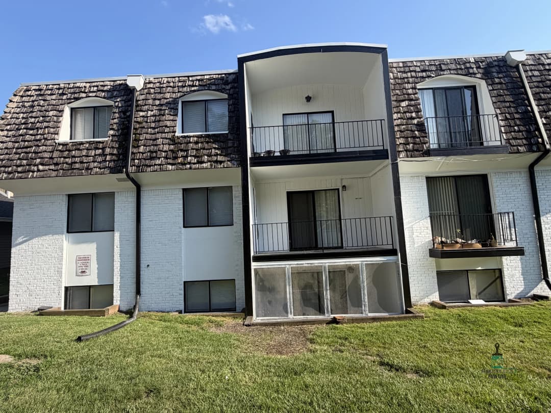 Modern apartment building with a grassy area and balconies, featuring a unique shingle roof.