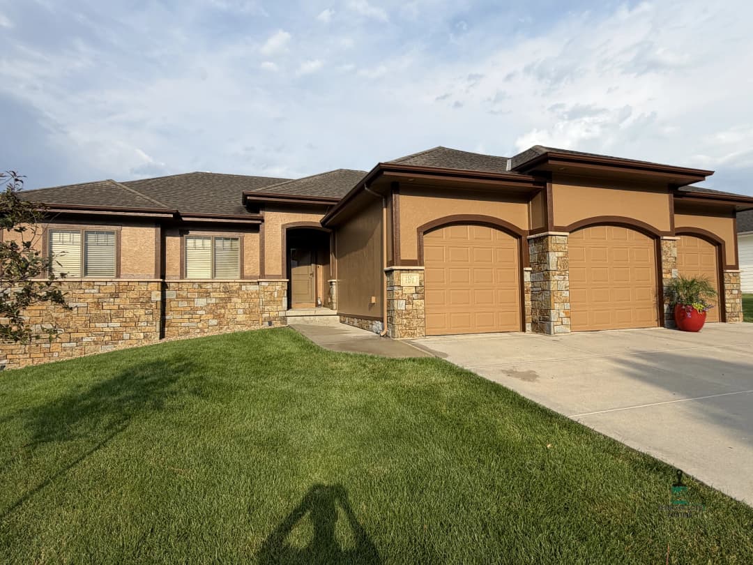 Modern single-family home with stone accents, two garage doors, and lush green lawn.