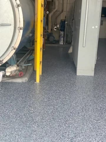 Industrial flooring in a facility with blue epoxy finish and machinery in background.