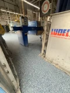 Industrial floor with blue epoxy coating and manufacturing equipment in a spacious facility.