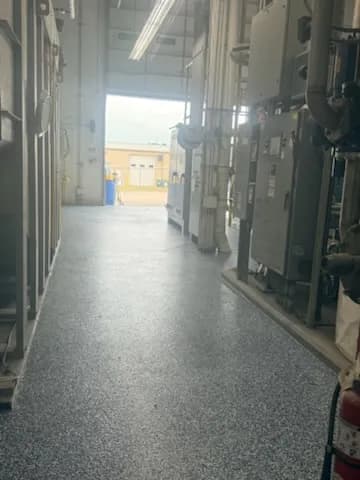 Industrial corridor with blue flooring and machinery, leading to an outdoor area.