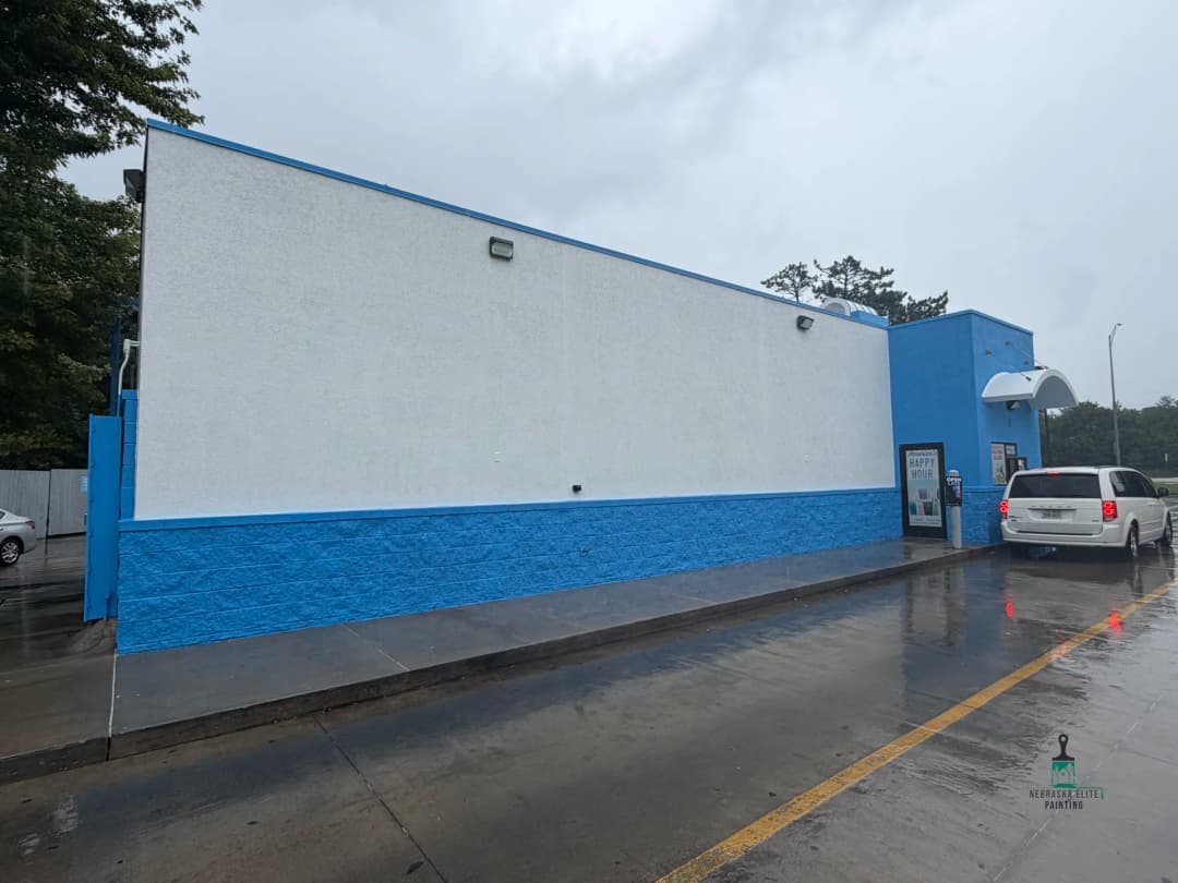 Fast food restaurant exterior with blue and white design, wet pavement, and cloudy sky.