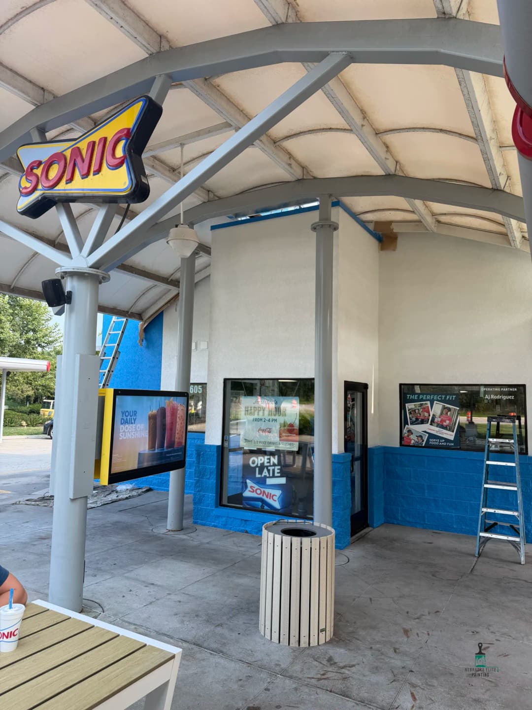 Sonic Drive-In exterior with outdoor seating, promotional signs, and ladder for maintenance.