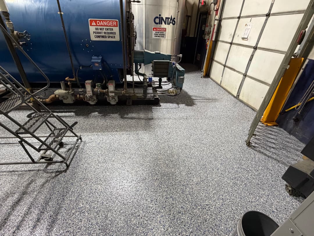 Industrial workspace featuring a blue tank, equipment, and epoxy flooring. Safety warning visible.