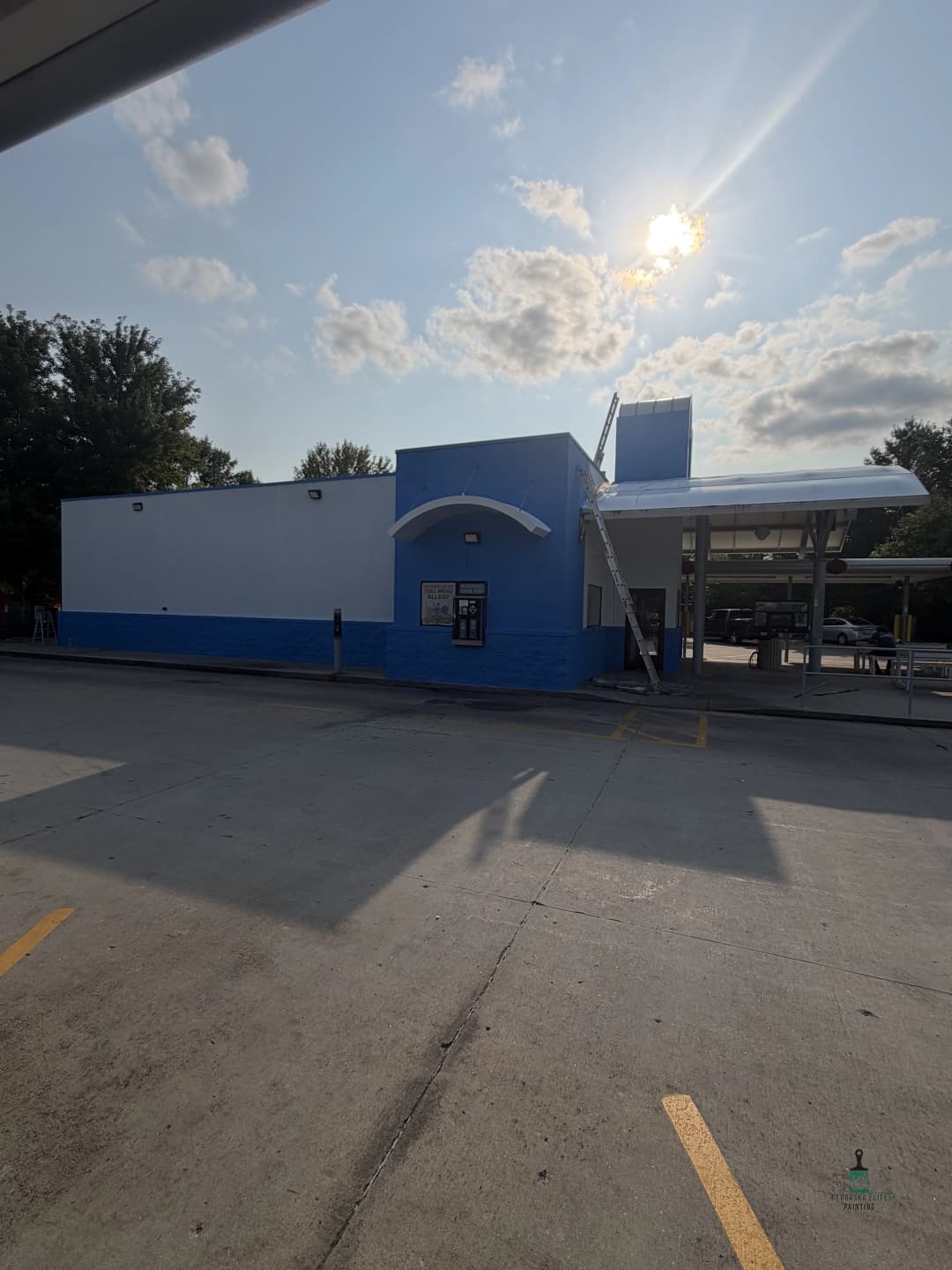 Blue and white commercial building with sunlight, outdoor canopy, and parking lot.