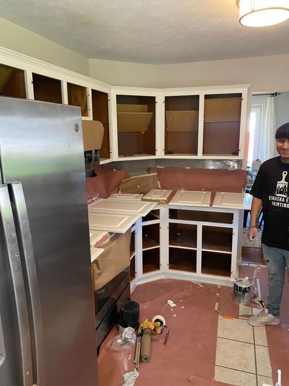 Kitchen renovation in progress with open cabinets and a worker painting.