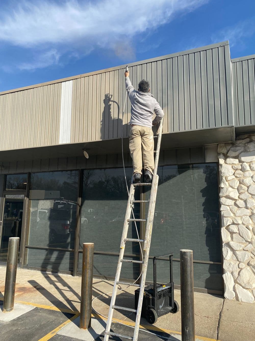 Man on ladder painting building exterior with blue sky in background.