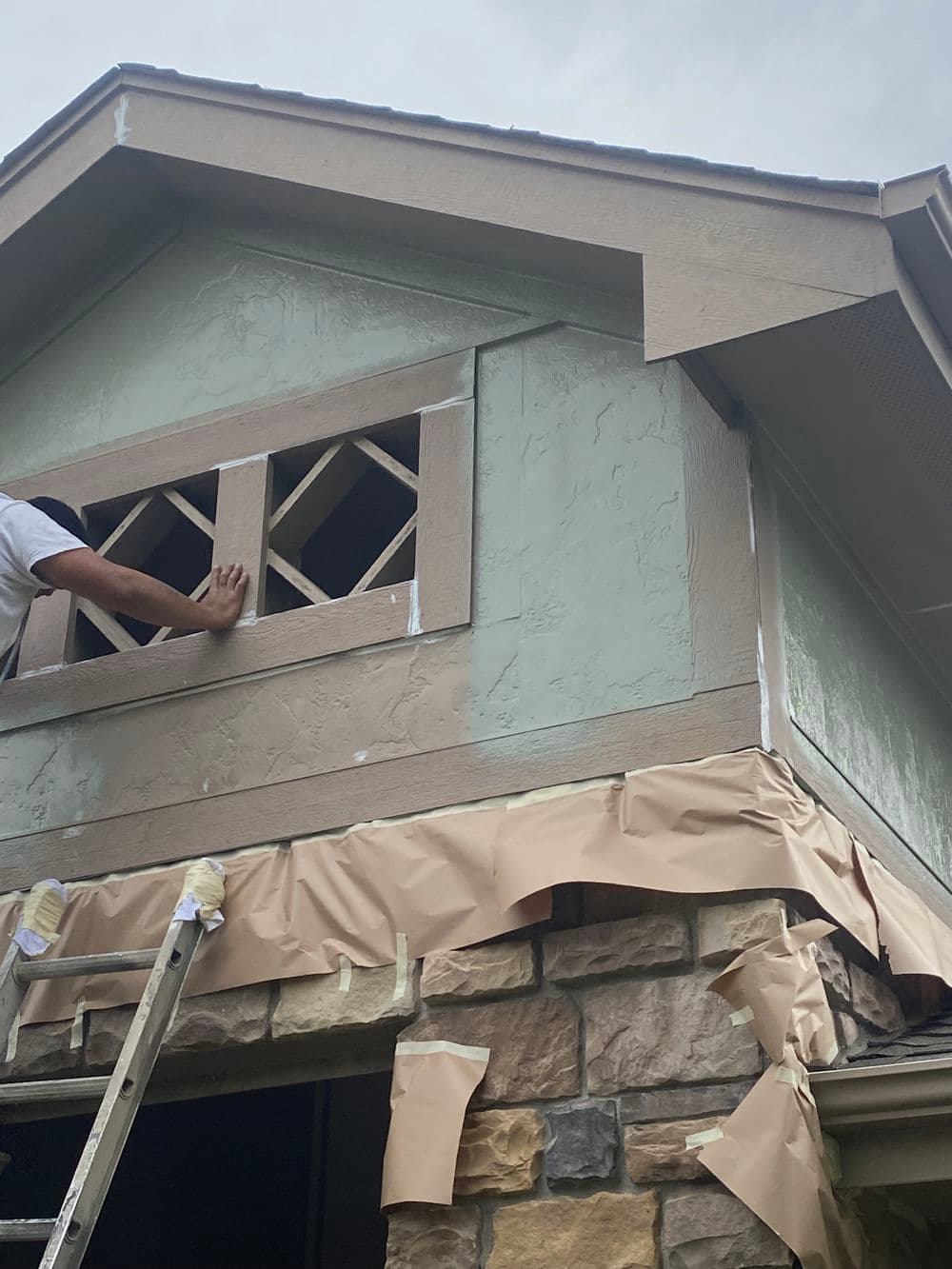 Worker repairing exterior house with ladder, focusing on window and siding details.