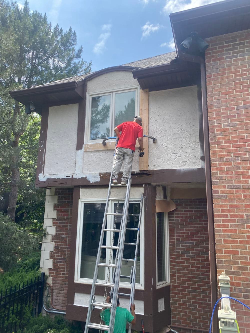 Person painting a home's exterior with a ladder, showcasing house renovation in progress.