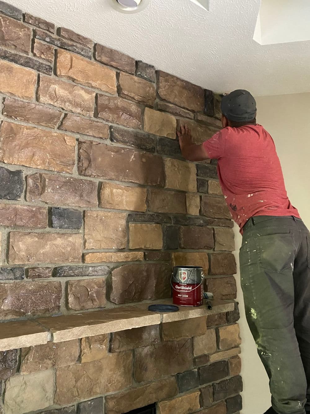 Man installing stone on a fireplace wall with a paint can nearby, showcasing home improvement skills.