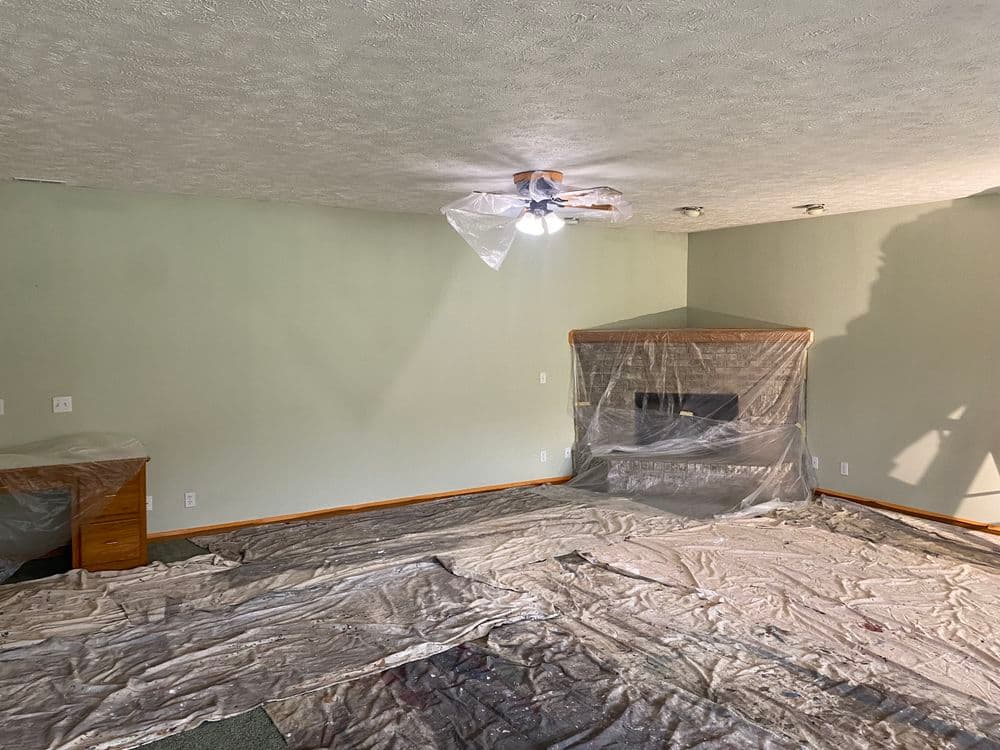 Living room under renovation with plastic covering furniture and floor, highlighting preparation work.