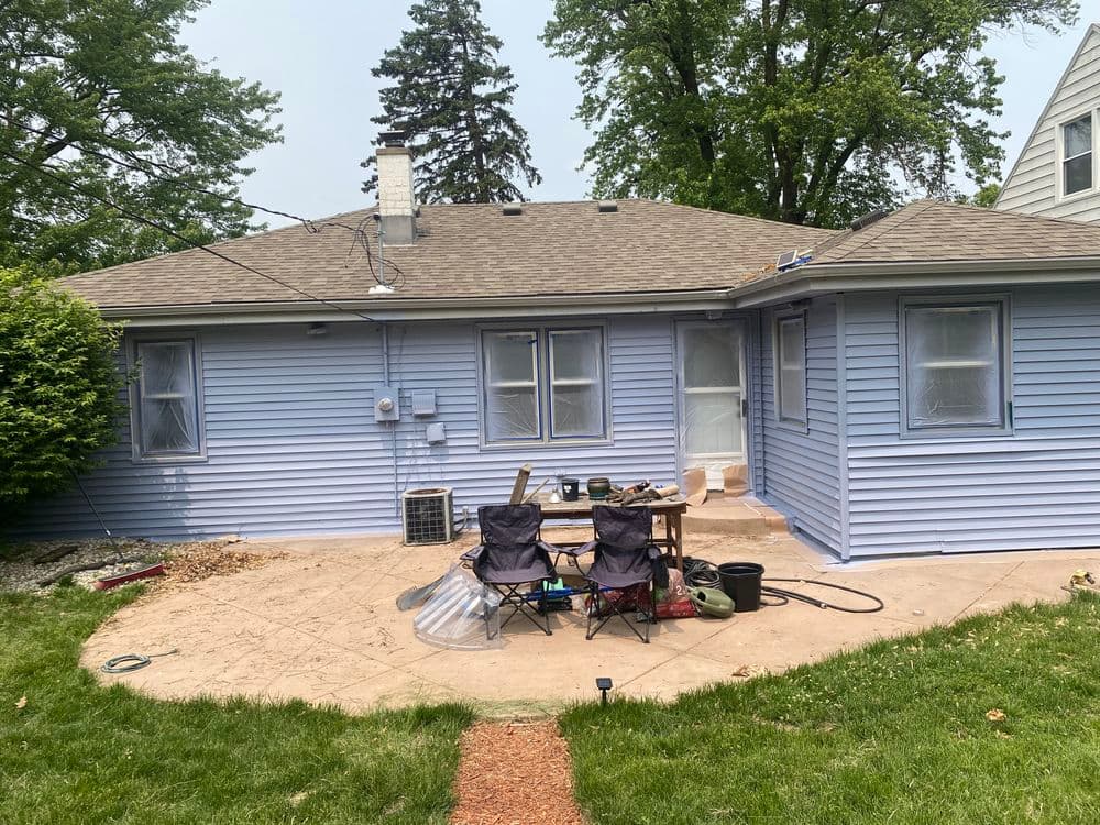 Light blue house with patio, gardening tools, and two chairs in the backyard.