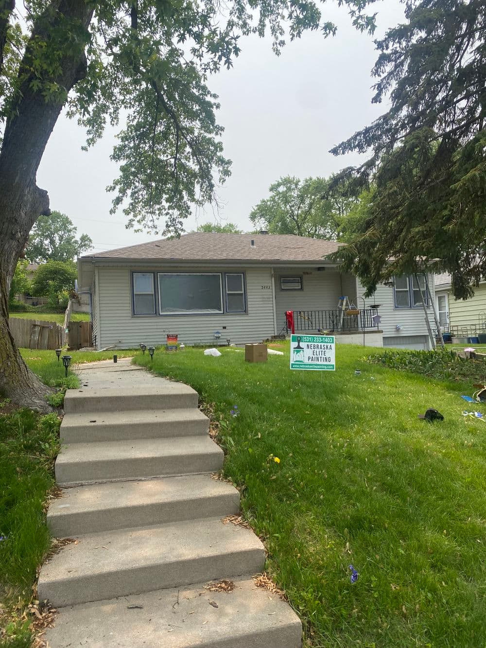 Single-family home with green lawn and front steps, featuring a real estate sign.