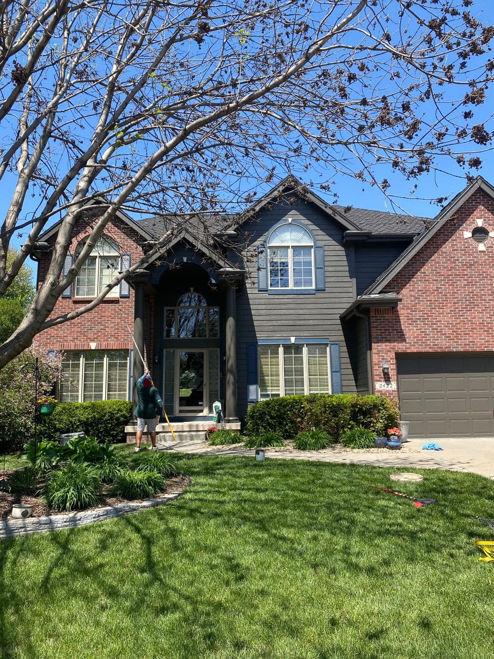 Family home with brick and siding exterior, landscaped yard, and a person cleaning windows.