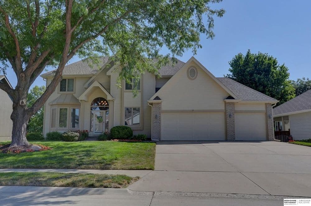 Elegant two-story house with a welcoming entrance, lush landscaping, and a two-car garage.
