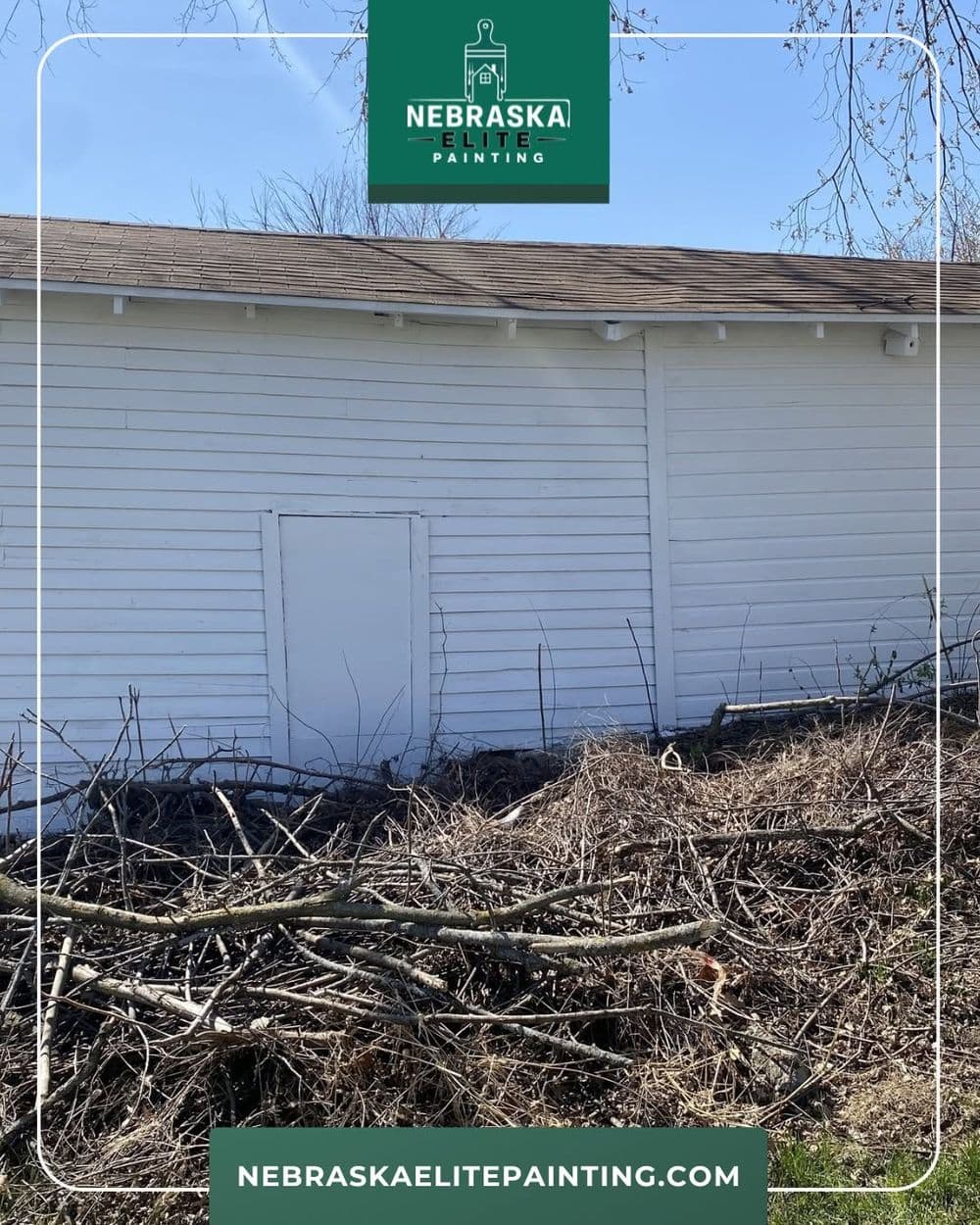 White exterior wall of a building with shrubs and branches in the foreground. Nebraska Elite Painting.