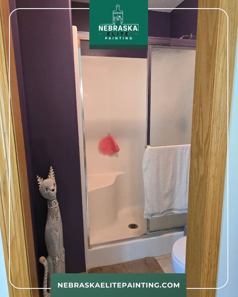 Bathroom with purple walls, glass shower door, towel, and decorative figure. Nebraska Elite Painting.