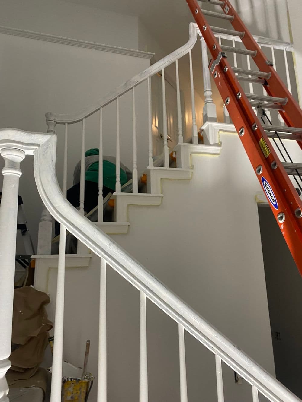 Person painting staircase with ladder and tools in a home interior.