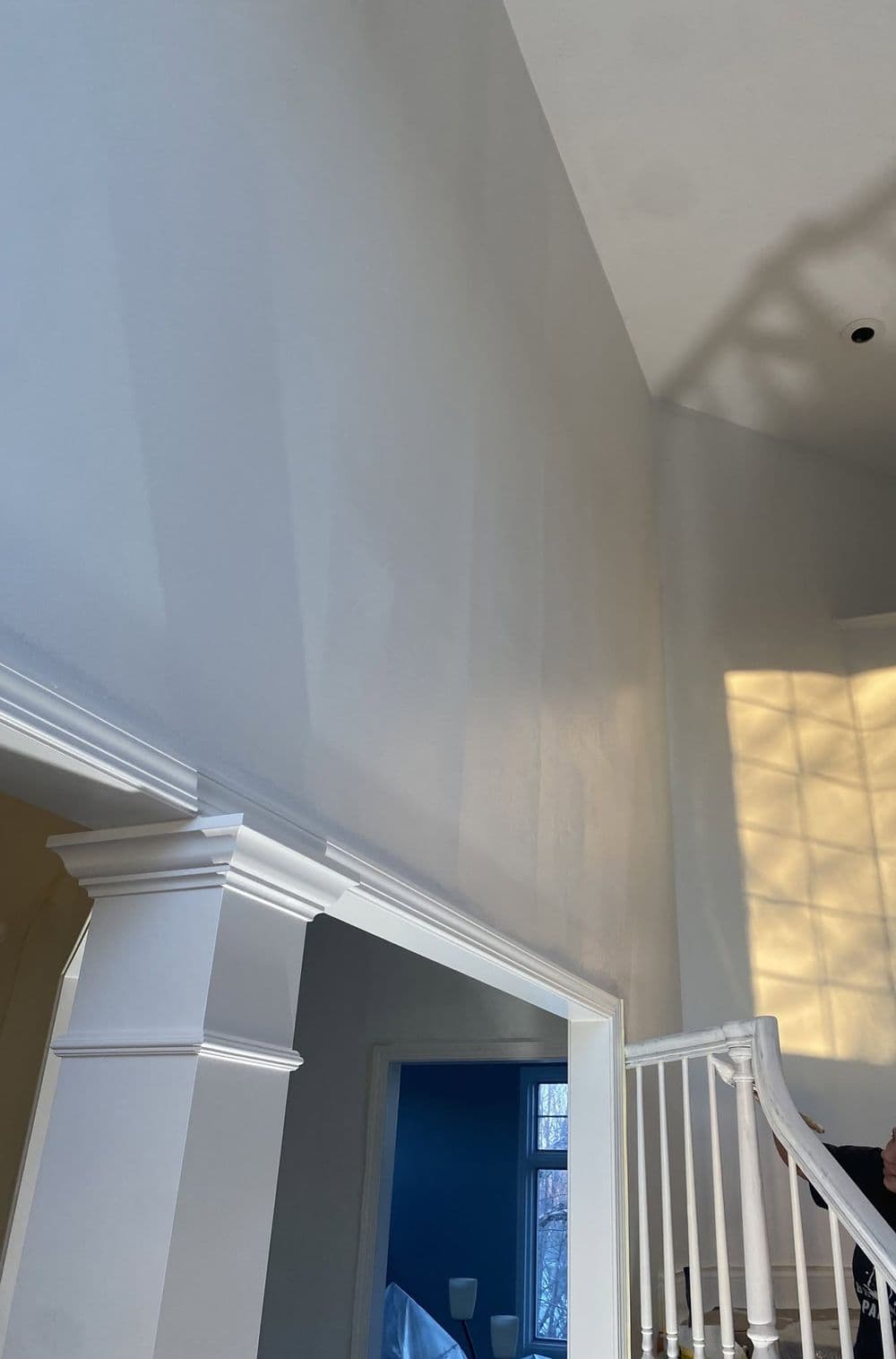 Bright, freshly painted tall wall in a home with architectural trim and sunlight shadows.