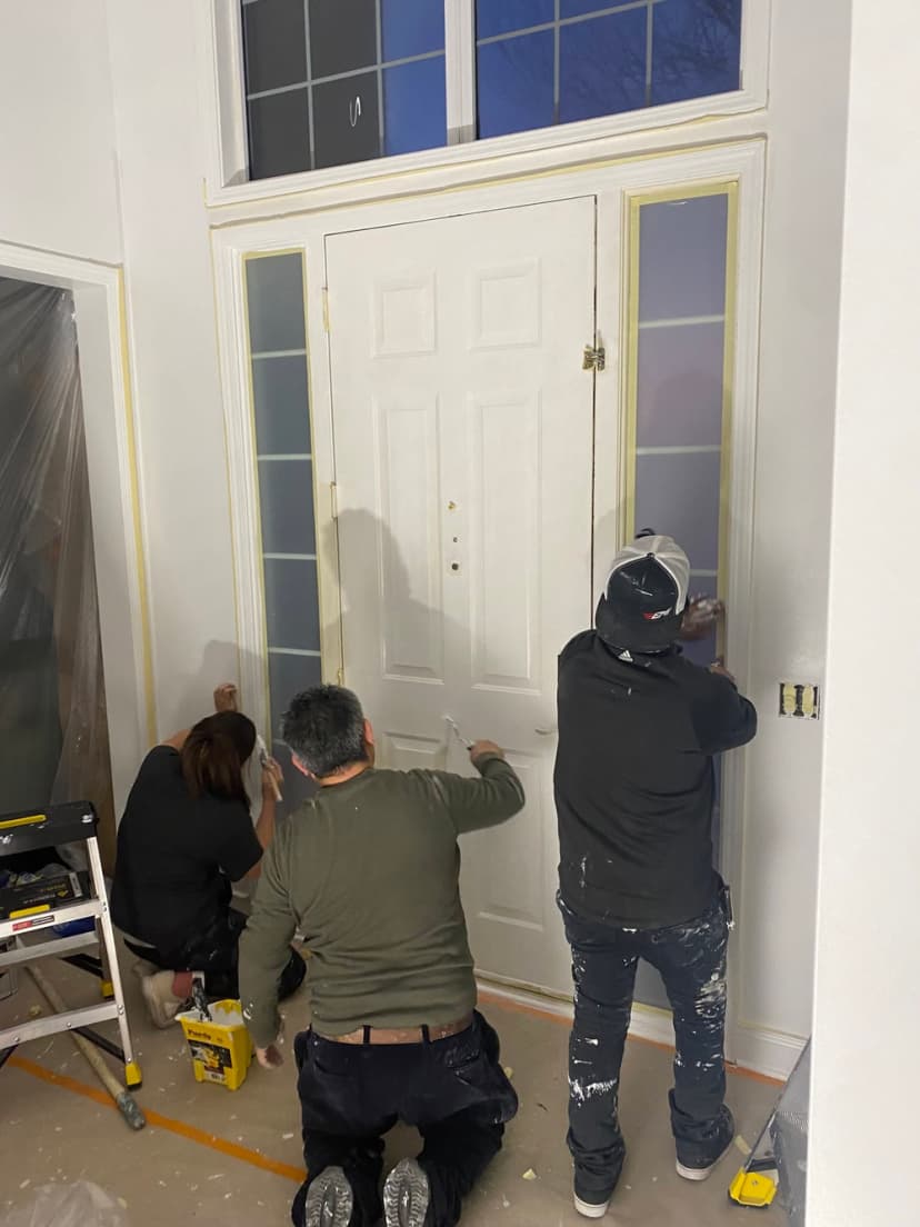 Three painters preparing and painting a front door in a home renovation project.