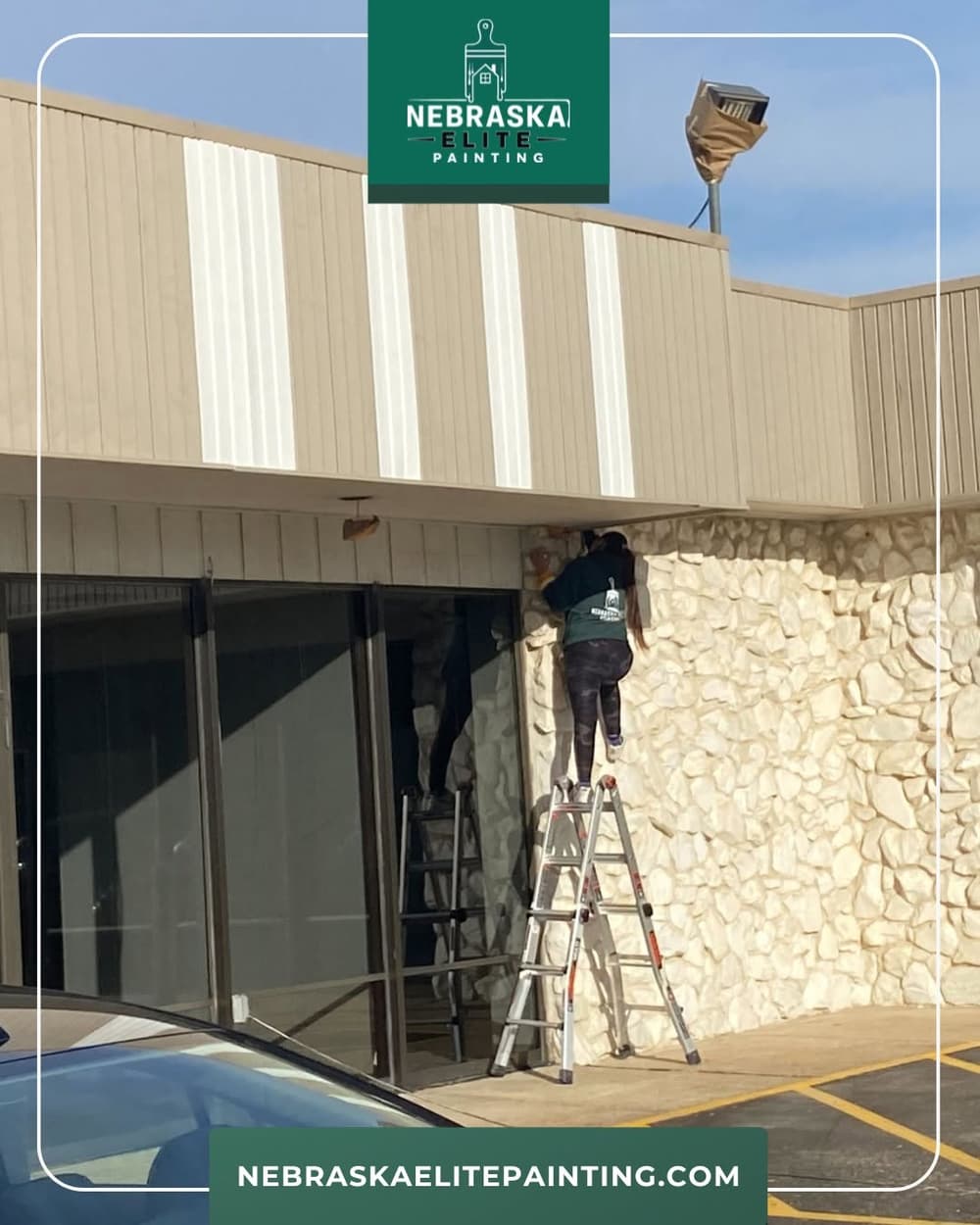 Painter using a ladder to work on a building's exterior wall, showcasing Nebraska Elite Painting services.